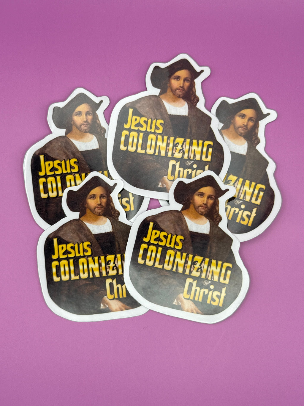 A stack of die-cut stickers featuring a parody art print of Jesus Christ dressed as Christopher Columbus, with the bold yellow text 'Jesus Colonizing Christ'. The stickers are arranged on a solid pink background.